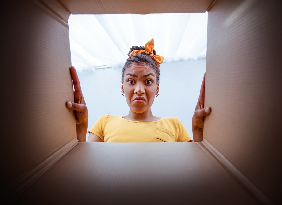 Bad Delivery Service Concept. Angry dissatisfied black woman unpacking and looking in cardboard box, received damaged item, feeling upset with wrong parcel, view from the inside of package