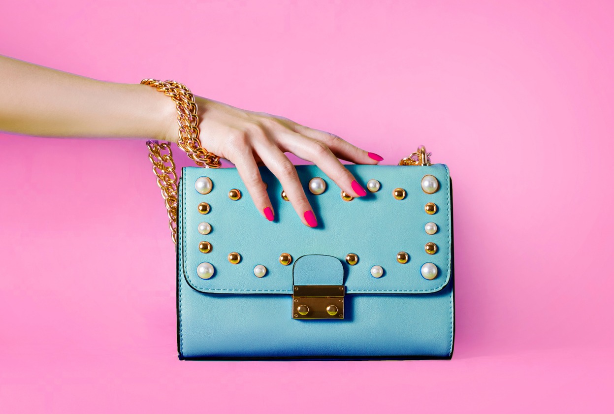 Sky blue handbag purse and beautiful woman hand with red manicure isolated on pink background