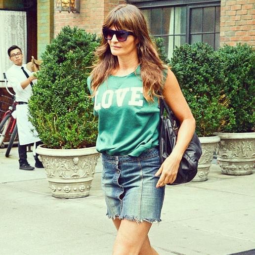 Helena Christensen in street style, man in a shirt at the back, big potted plants, brick building