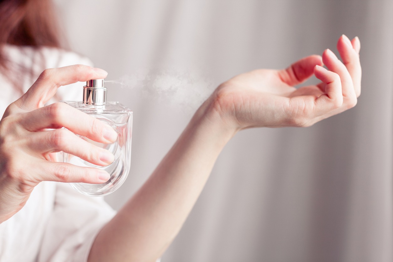 A girl in a white dress sprays herself perfume on her wrist