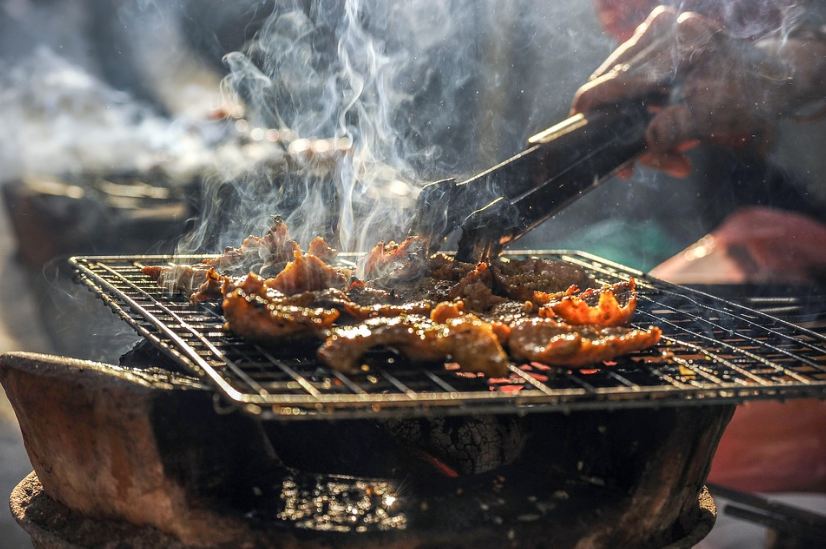 a person barbecuing meat on a grill, smoke