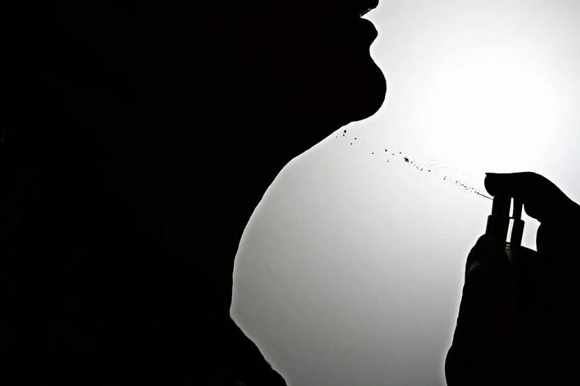 a silhouette of a person spraying themselves with perfume