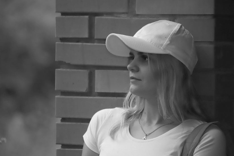 a woman leaning against a brick wall wearing a baseball cap