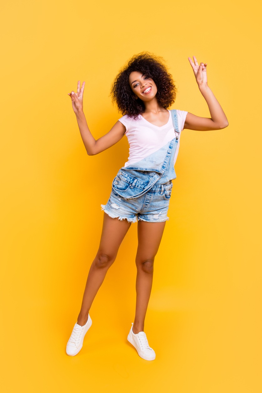 Vertical portrait of fullbody portrait of cool peaceful chick with beaming smile gesturing v-signs with two hands looking at camera isolated on yellow background
