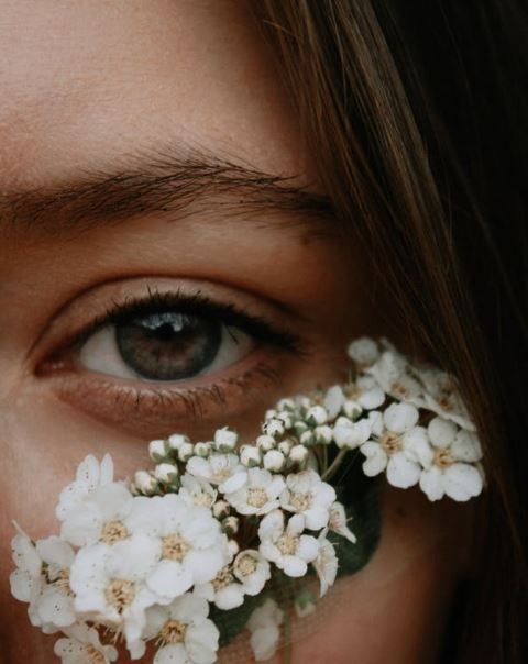a close-up of a woman’s eye and brow with flowers under her eye