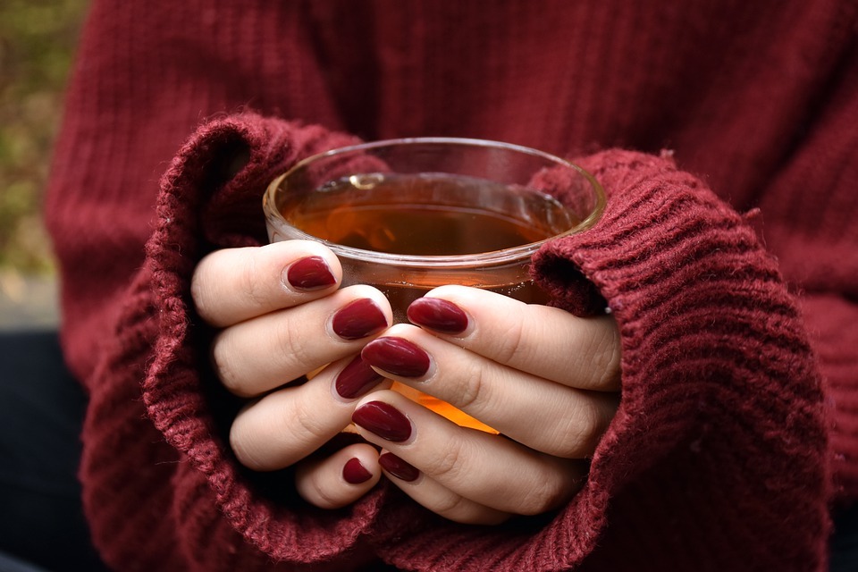 a person wearing a sweater holding a cup of tea