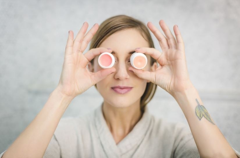 a woman holding two lip balms against her eyes