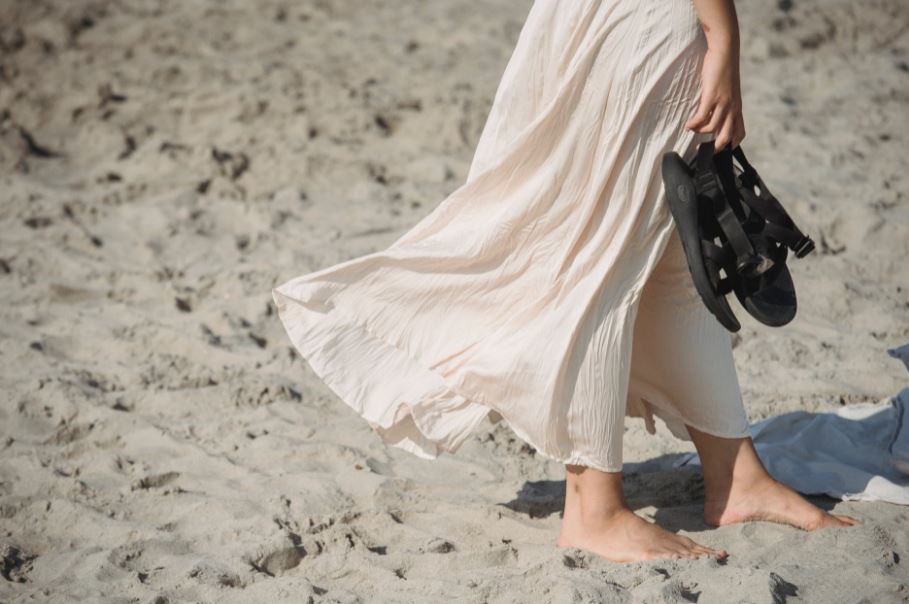 a woman walking on sand and holding her sandals