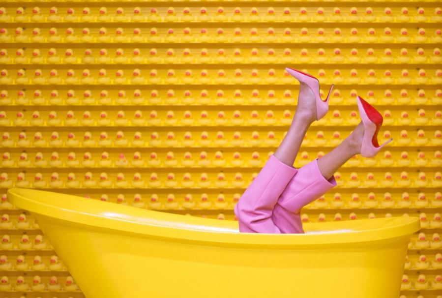 legs of someone wearing heels inside a yellow bathtub, a wall full of yellow rubber ducks