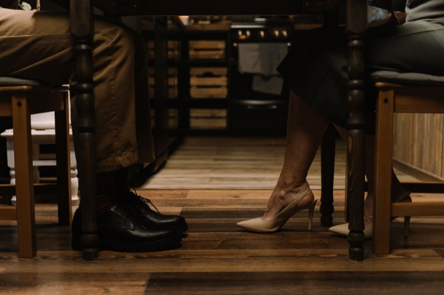 the feet of a man and woman under the table, a woman wearing heels, wooden chairs