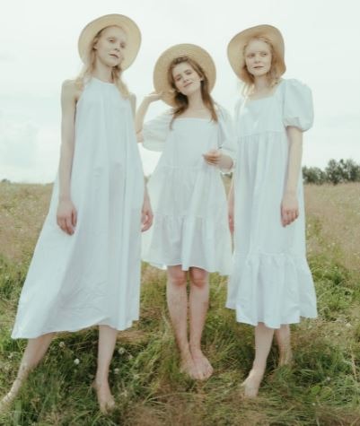 three women wearing white dresses standing on a field