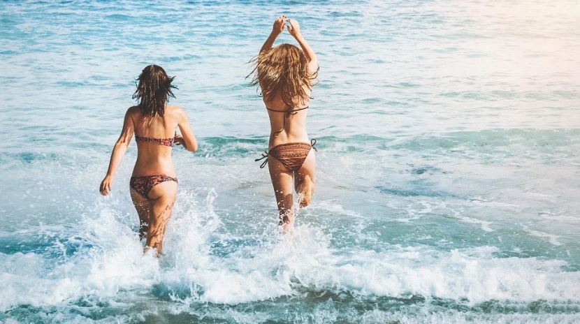 two women wearing bikinis enjoying the water, beach waves