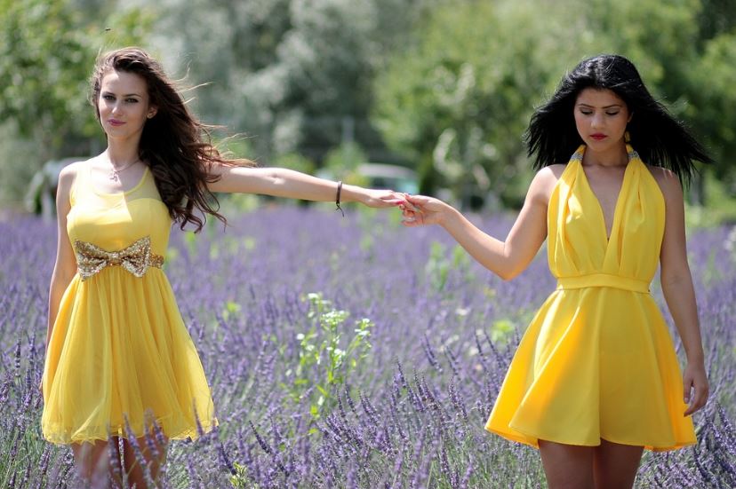 two women wearing yellow dresses holding hands in a lavender field