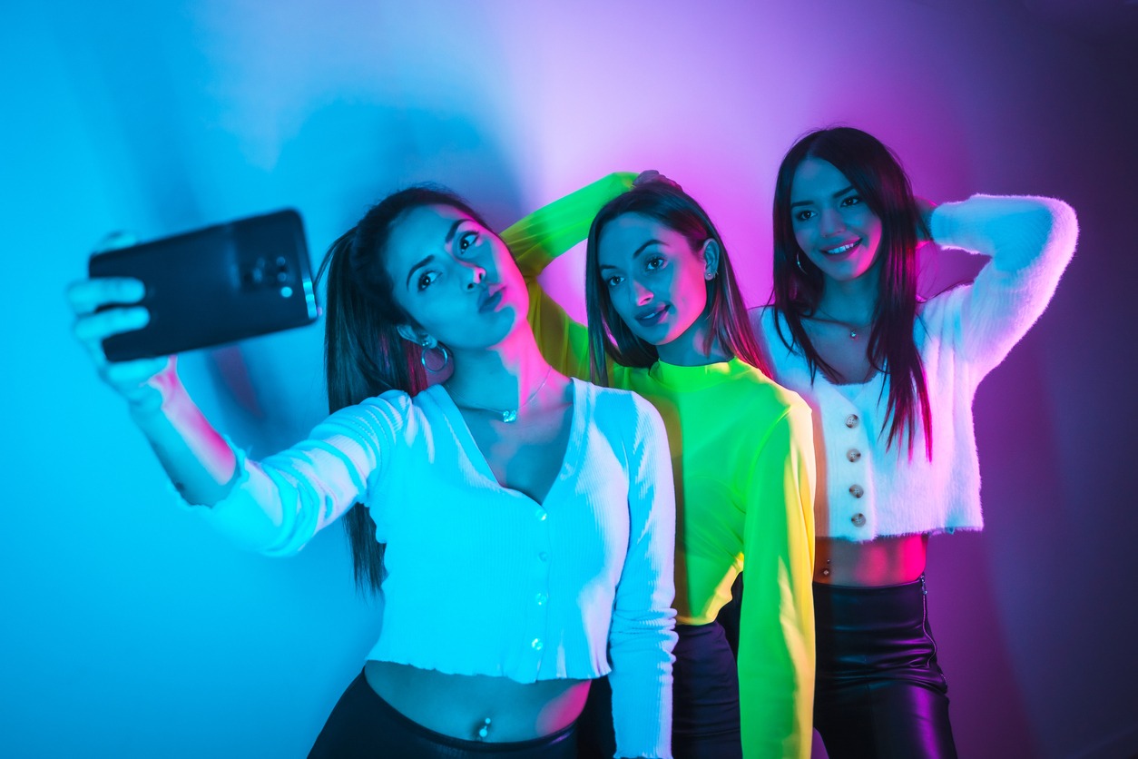 Lifestyle of friends partying in a nightclub with blue and pink neon lights, taking a selfie with the phone