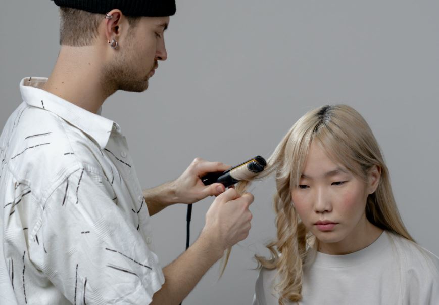 a male hairstylist curling a woman’s hair