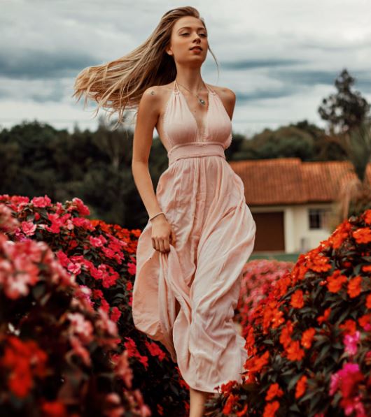 a woman in a dress passing through a field of flowers