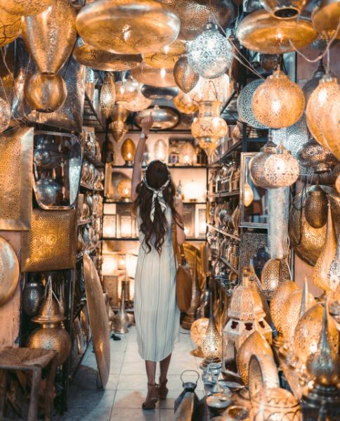 a woman in white dress standing, choosing some steel, brass home decors