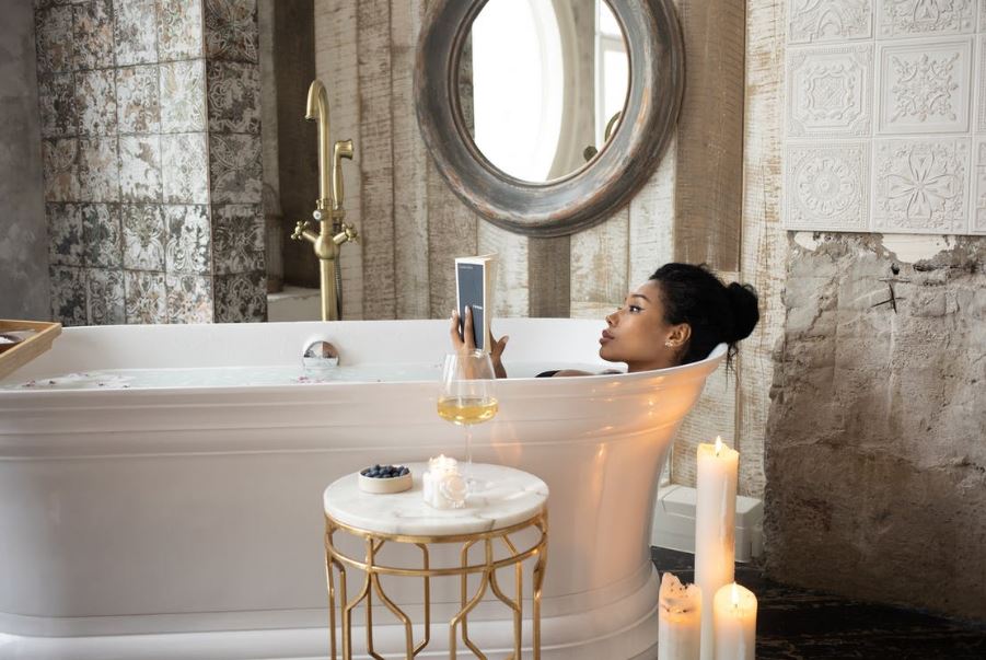 a woman reading a book while taking a bath, candles, fruits, champagne