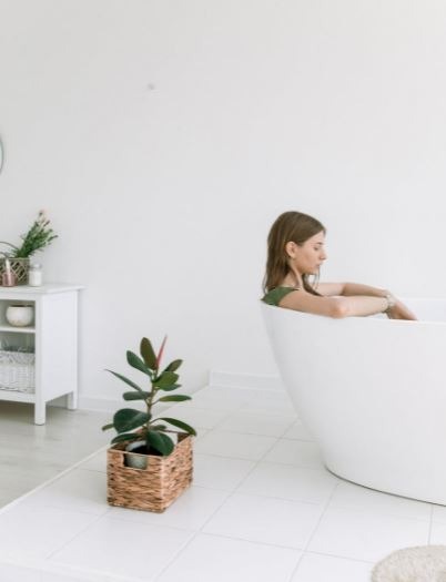 a woman soaking in the bathtub, plants, table