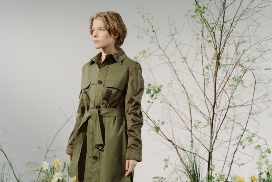 a woman wearing a trench coat standing near a tree