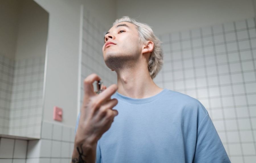 man spraying perfume on himself inside the bathroom