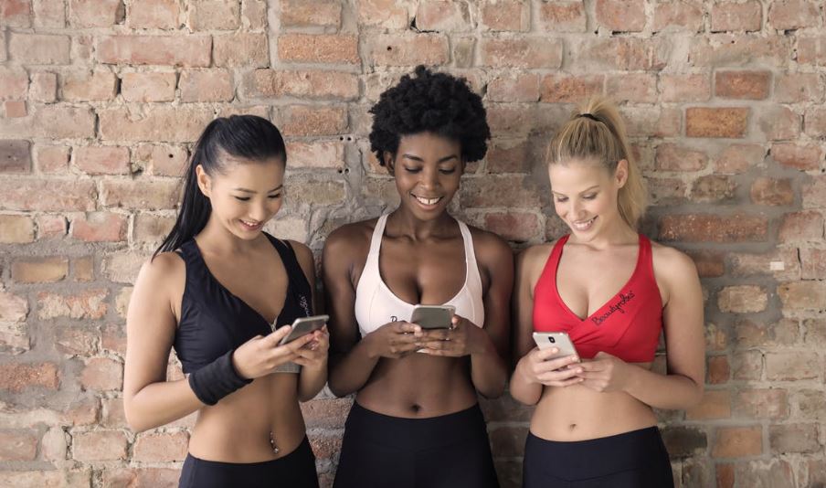 three women wearing workout clothes while looking at their phones