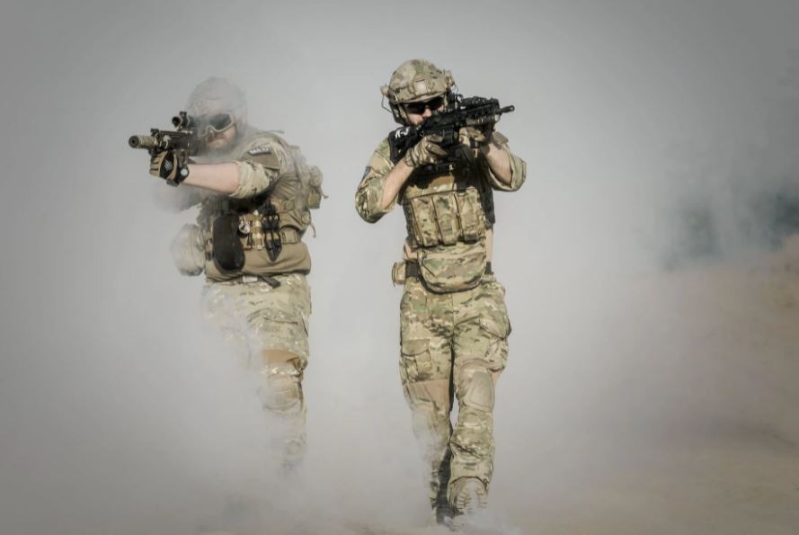 two soldiers in camouflage uniforms holding guns and surrounded by smoke