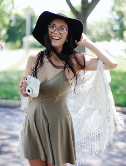 a woman in Bohemian fashion get up (flowy dress, shawl, and a hat) holding a polaroid camera