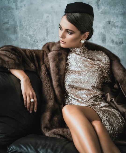 a woman sitting on a sofa wearing a fur coat over a sequined dress