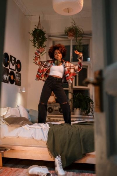 a woman wearing a plaid shirt and ripped jeans while dancing on top of her bed