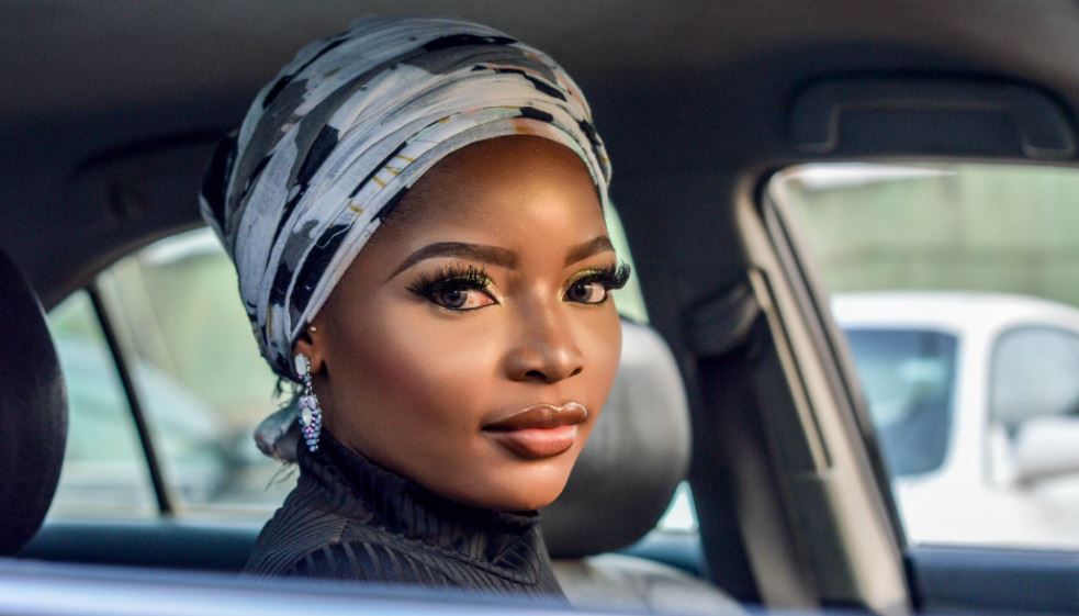 a woman wearing white and black floral headscarf inside a car with defined eyelashes