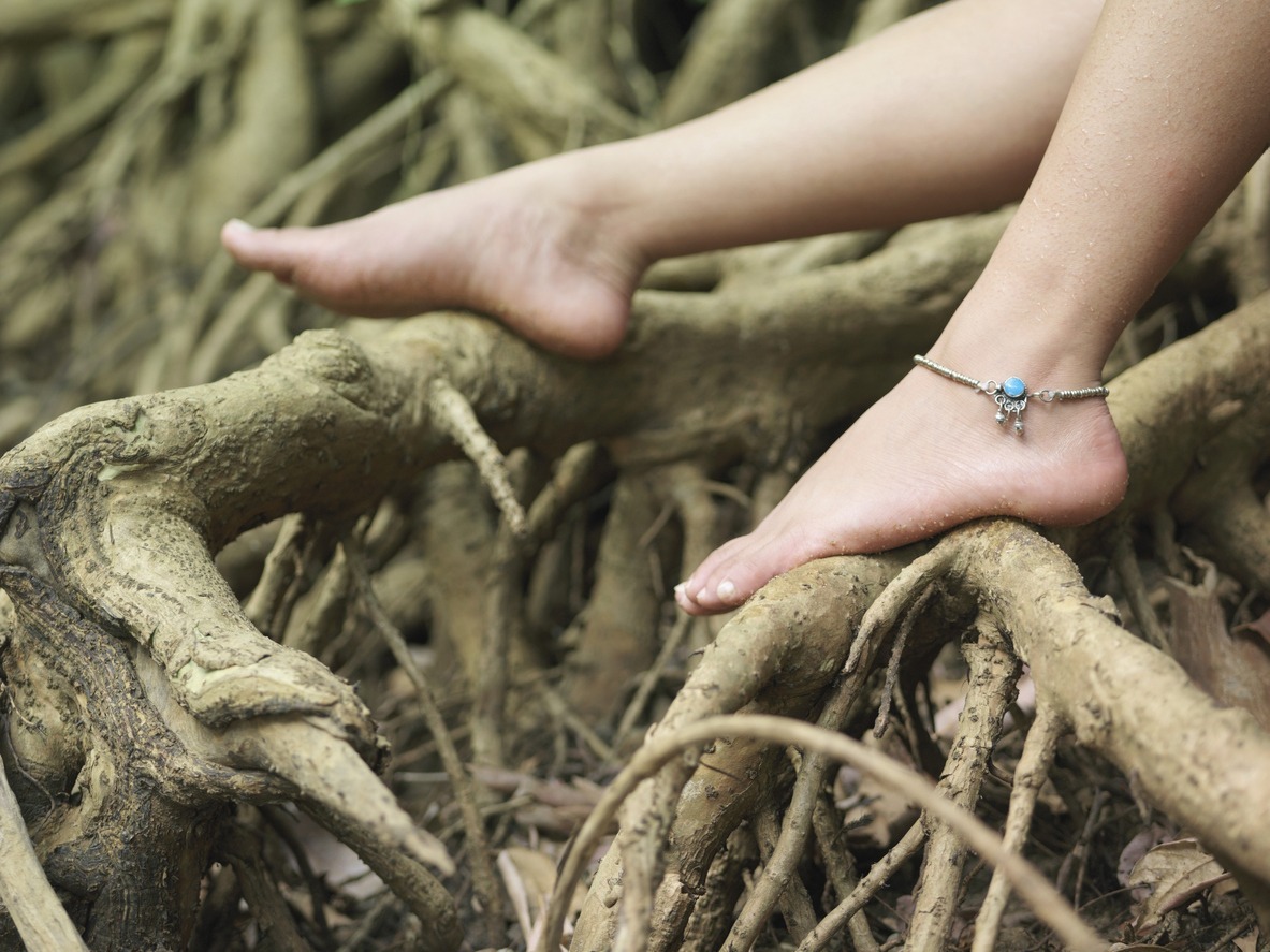 closeup of a young woman's bare feet with an ankle bracelet on roots