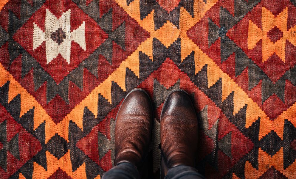 the leather shoes of a person standing on a patterned rug