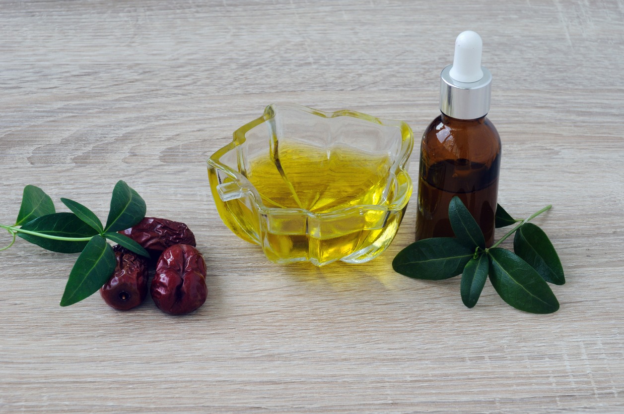 Jojoba oil in a transparent vase, fruits and natural leaves, a bottle of oil on a wooden table.