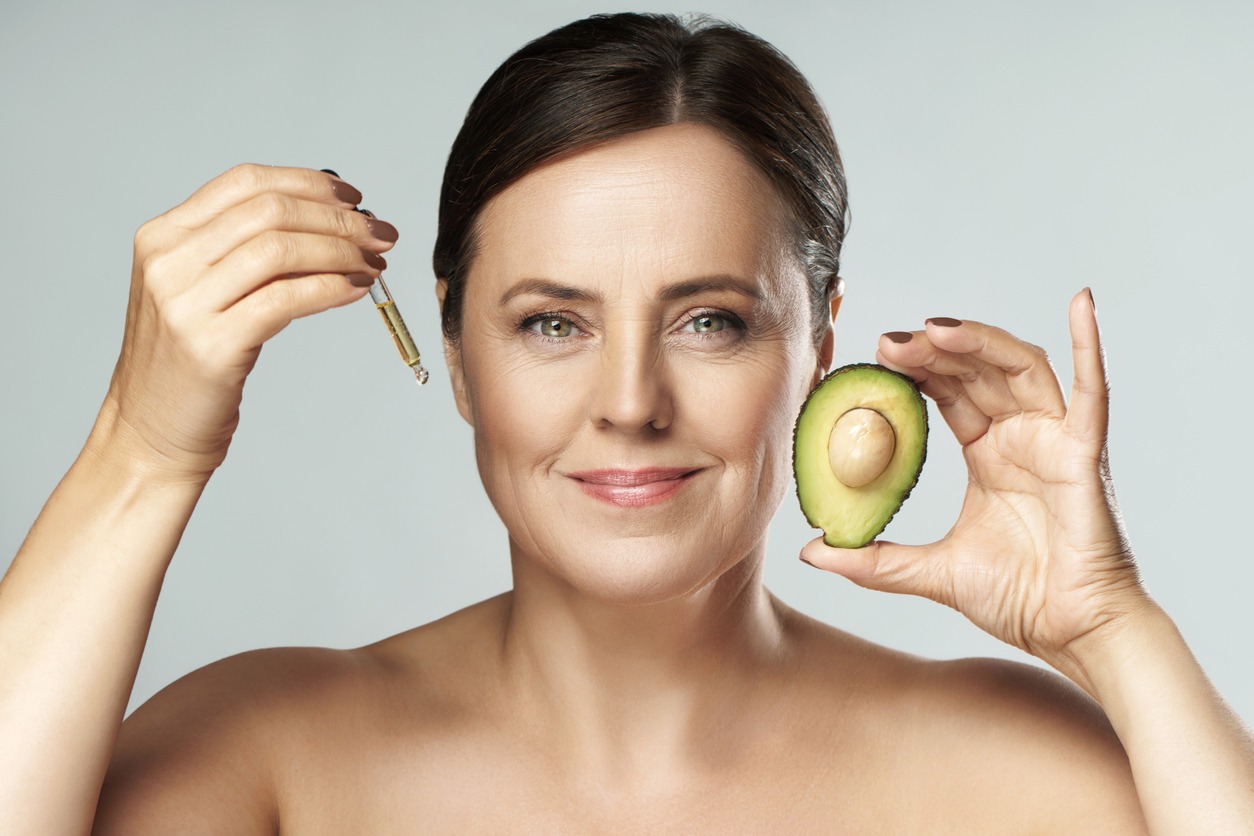 Beautiful middle aged woman holding dropper with avocado oil