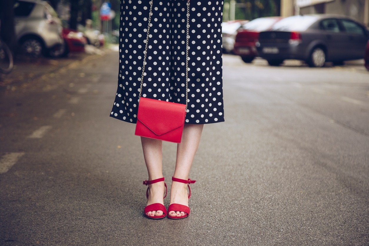 a woman in a polka dot dress and red high heel shoes holding a red purse