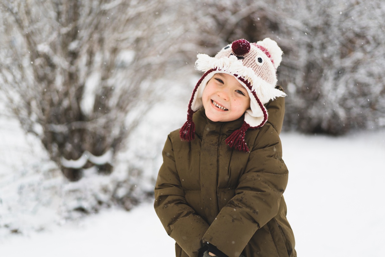Child enjoying winter. Cute little boy in funny winter hat walks during a snowfall. Outdoors winter activities for kids.