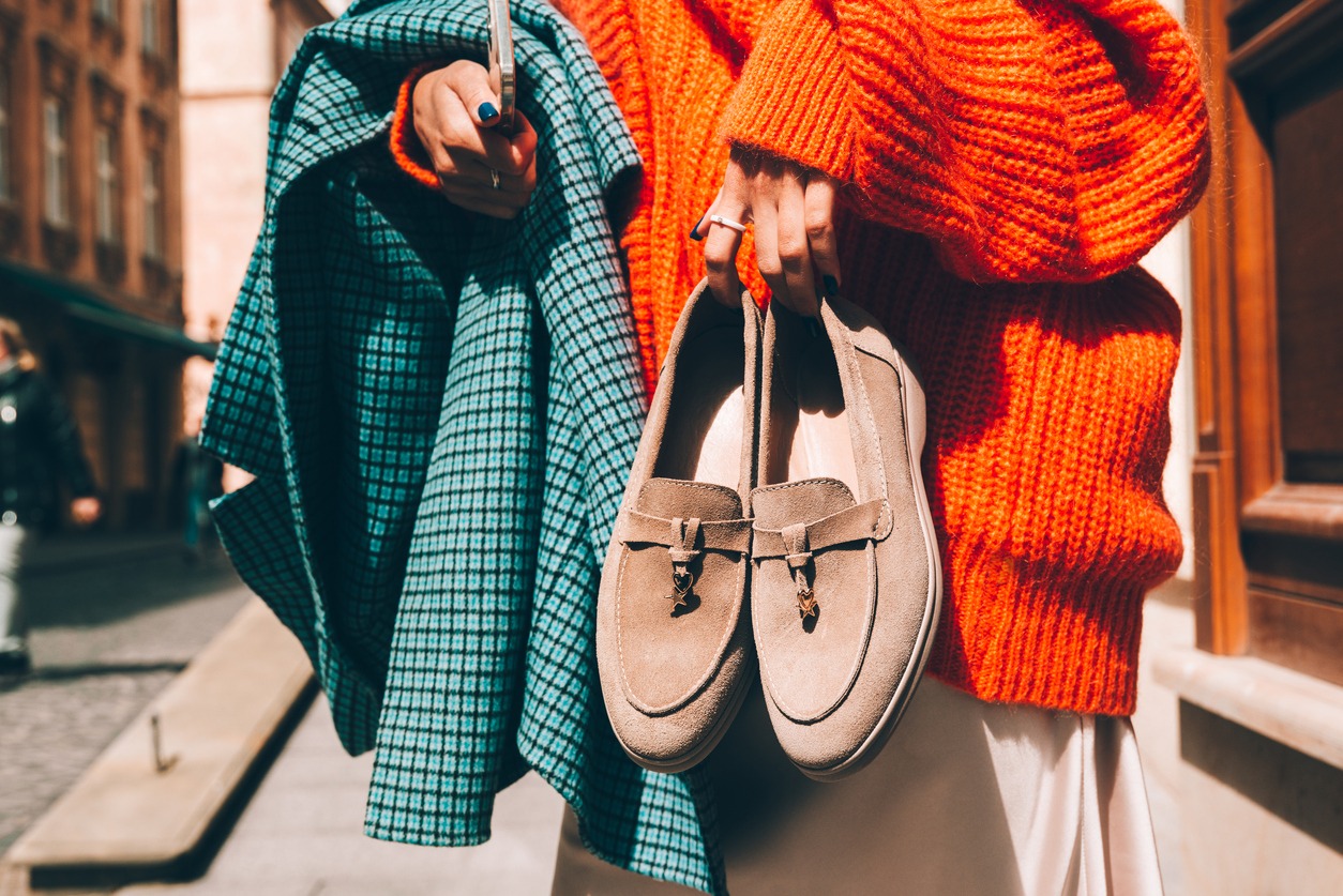 Close-up photo of fashionable women in orange sweater and beige dress holding in hands checkered coat and beige suede shoes