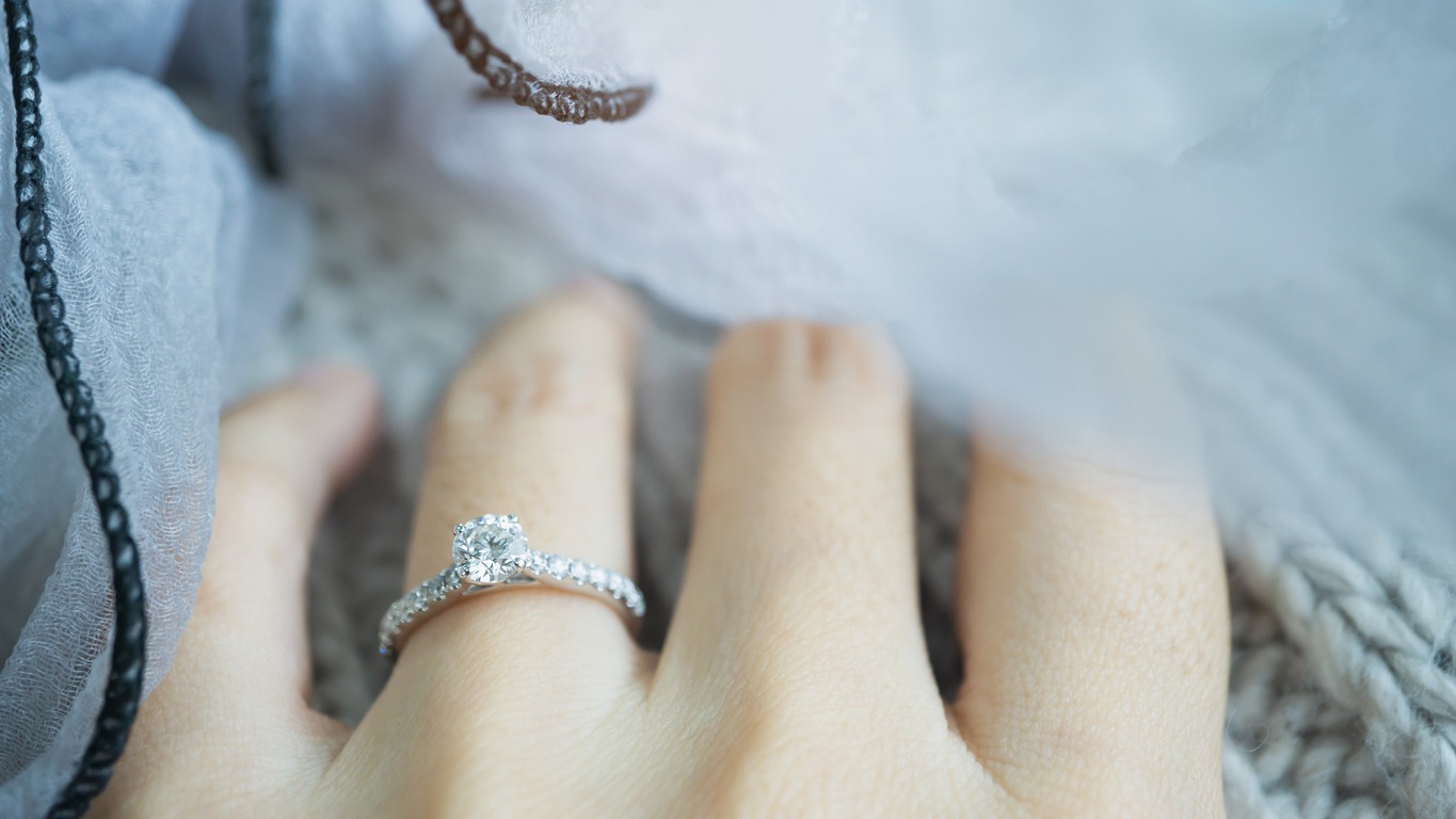 Close-up of an elegant diamond ring on a woman's finger with a gray knit background. love and wedding concept. Soft and selective focus