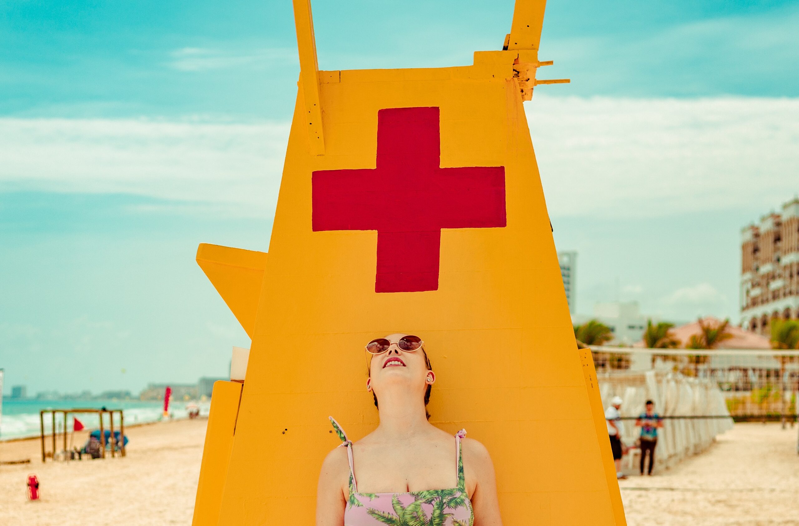 a woman wearing sunglasses looking at something overhead while standing near a lifeguard tower at the beach