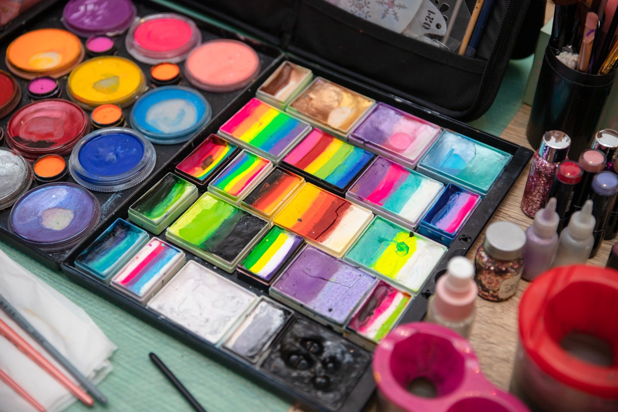 Colourful paint boxes and tubes with paints on a table. Paints and brushes for make-up, for painting on faces, face painting, face art. Abstract background and texture.