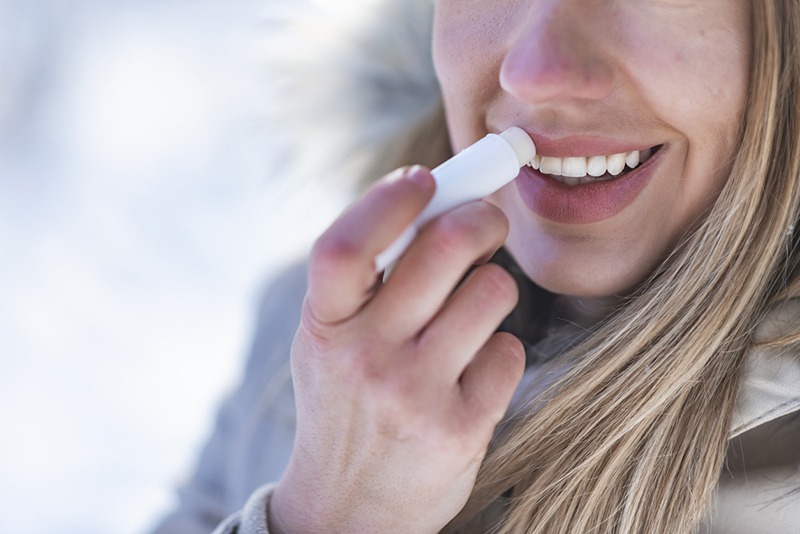 cropped photo of a young female applying lip balm in winter