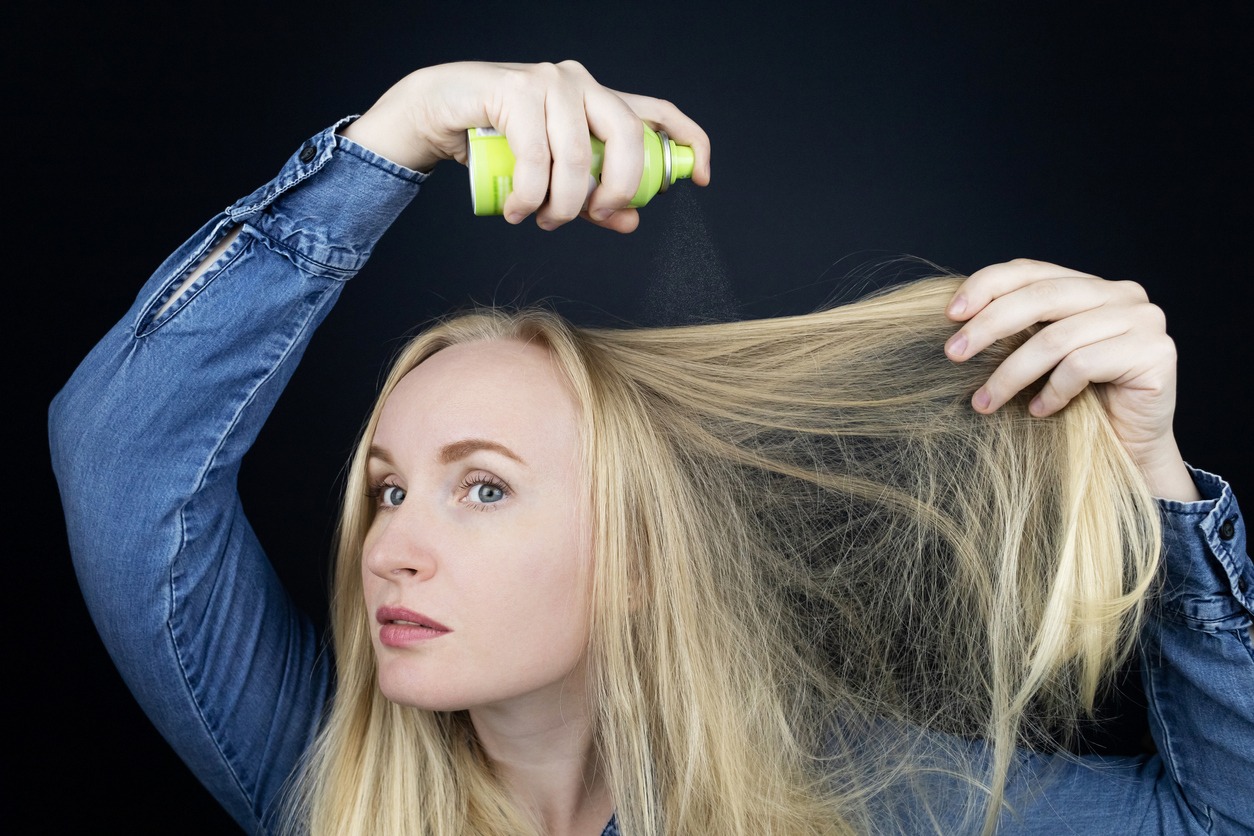 Dry shampoo. Blonde girl sprays shampoo on her hair. The problem of oily hair while traveling. An emergency remedy for excessive sebum production. Make your head clean without water