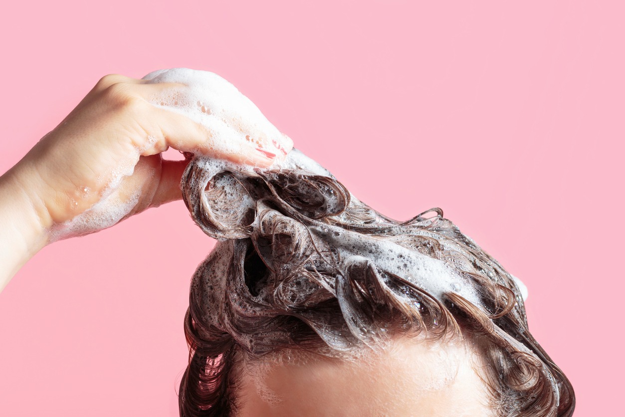 A girl washes her hair with shampoo on pink background, front view