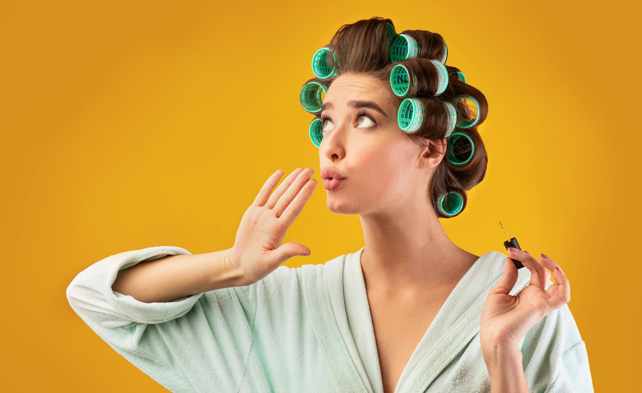 Glamorous Housewife With Curlers Blowing At Polished Nails, Studio Shot