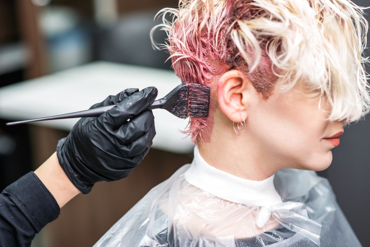 Hairdresser hand in black gloves paints the woman's hair in a pink color