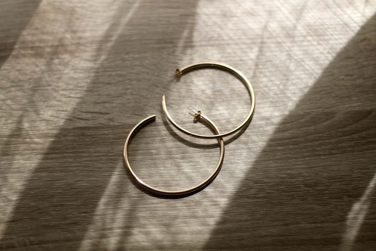 Golden hoop earrings on wooden background, illuminated by sunlight. Selective focus