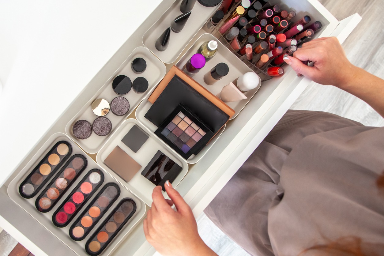 Woman hands neatly organising makeup and cosmetics in the drawer of vanity dressing table