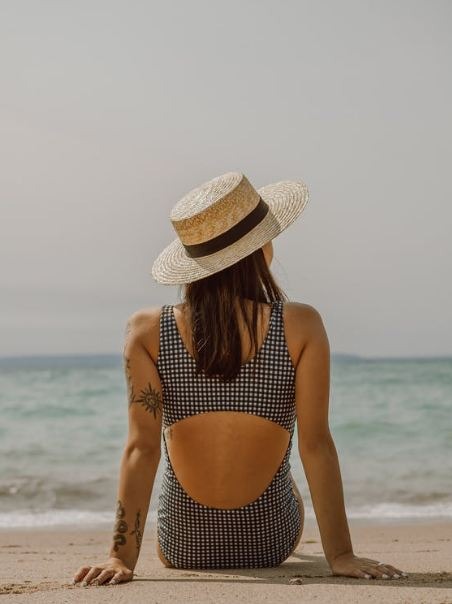 woman-with-tattoos-in-swimsuit-and-hat-resting-on-sandy-beach