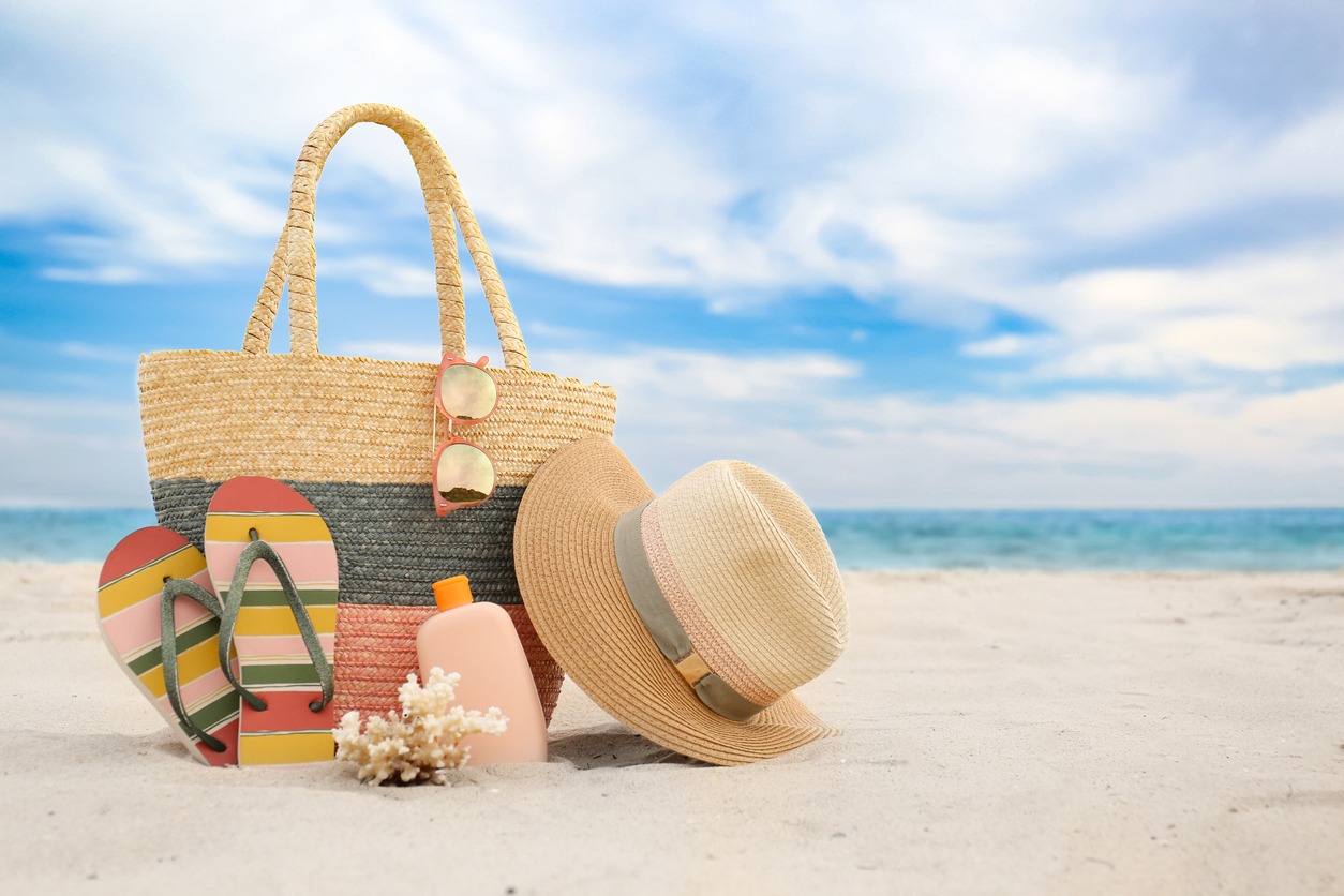 A beach bag with different stylish beach objects on the sand